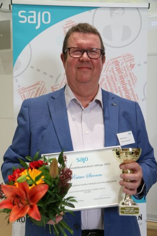 Rehtori Raimo Sivonen kunniakirja, pokaali ja kukkakimppu kädessä.